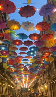 many colorful umbrellas are hanging from the ceiling in an alleyway at night time