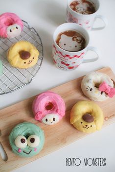 there are donuts with faces on them and two cups of coffee in the background