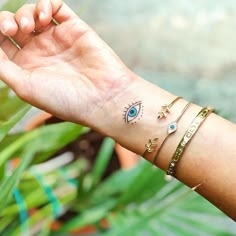 a woman's arm with three bracelets and an evil eye tattoo on it