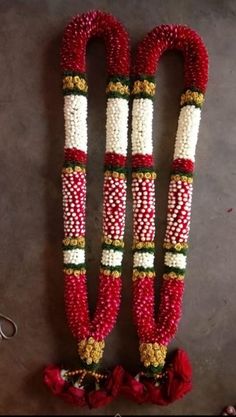 two red and white beaded garlands with flowers on the ground next to each other