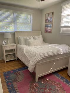 a white bed sitting on top of a wooden floor next to a pink and blue rug