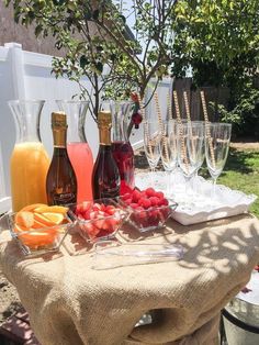 bottles and glasses are sitting on a table with strawberries, oranges, raspberries, and champagne