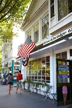 two people walking down the sidewalk in front of a building with an american flag on it