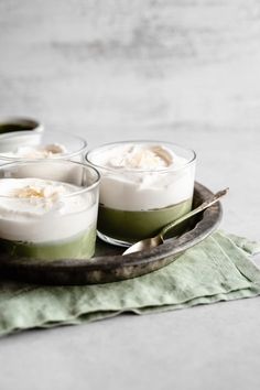 four desserts are sitting on a plate with spoons next to them and one is green