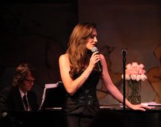 a woman sitting in front of a microphone on top of a table next to a vase with flowers