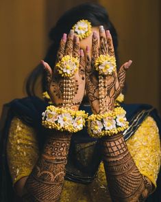 a woman with her hands covered in henna and yellow flowers on her face, holding her hands up to the camera