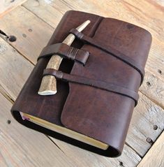 a brown leather journal with a wooden handle and two pens on the cover, sitting on a wood table