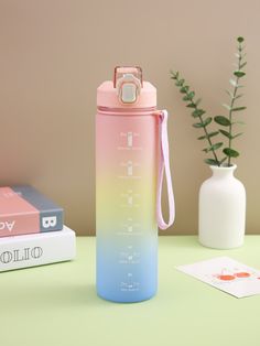 a pink and blue water bottle sitting on top of a table next to a plant