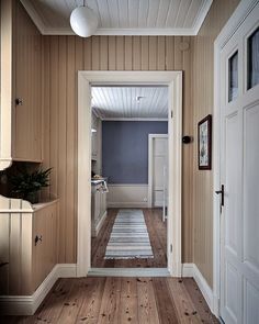 an empty hallway with wood paneling and white trim on the walls, leading to another room