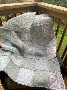 a quilted blanket sitting on top of a wooden chair next to a railing with trees in the background