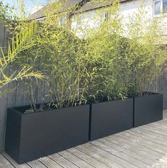 three black planters with plants in them on a wooden deck