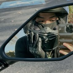 a woman taking a selfie in the side view mirror of a car while wearing a motorcycle helmet