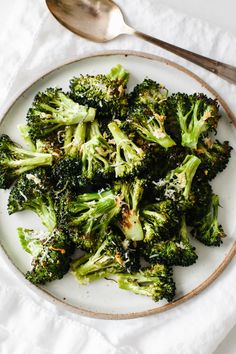 a white plate topped with cooked broccoli on top of a table next to a spoon