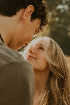 a man standing next to a woman with long blonde hair looking at her face and smiling