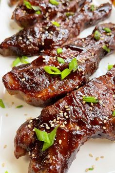 several pieces of meat on a white plate with sesame seeds and green garnishes