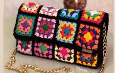 a multicolored crocheted purse on a chain with a vase in the background