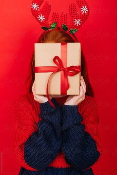 a woman with reindeer antlers on her head is holding a present in front of her face