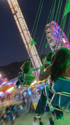 two people ride on swings at an amusement park during the night, while others watch