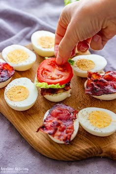 a person is picking up an egg and tomato sandwich on a wooden board with hard boiled eggs