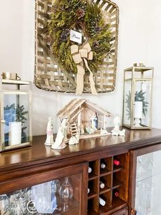 a christmas scene with a nativity scene on top of a hutch next to wine glasses and candles