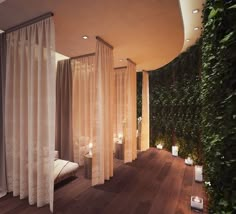 a room with sheer curtains and candles on the floor, next to a wall covered in greenery