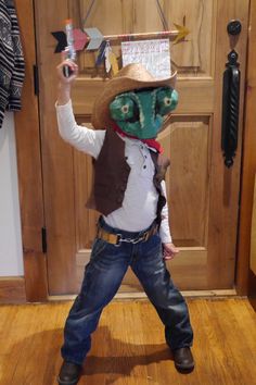 a young boy wearing a cowboy hat and vest holding up a cell phone in front of a wooden door