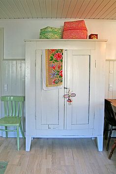 a white cabinet sitting in the corner of a room next to a table and chairs