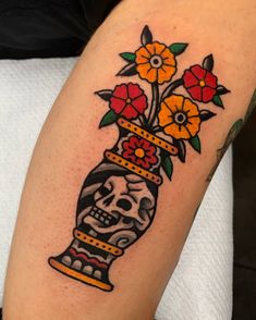 a skull and flowers in a vase tattoo on the right arm, with an orange flower