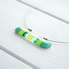 a green and yellow striped necklace on a white wooden surface with a cord attached to it