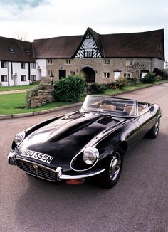 an old black sports car parked on the side of the road in front of a house