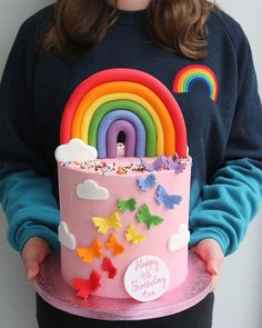 a woman holding a pink cake decorated with rainbows