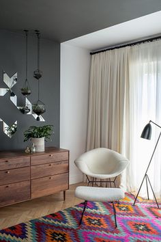 a living room with a colorful rug, chair and dresser in front of a window