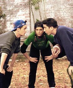 three people are playing with a football in the yard, and one person is wearing a helmet