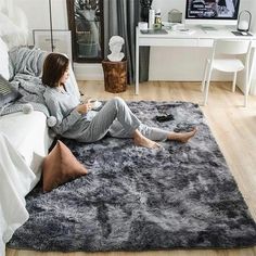 a woman laying on top of a gray rug in a bedroom next to a bed