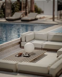 a white couch sitting next to a swimming pool near a lounge chair and table with an egg on it