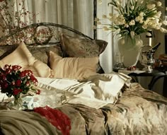 a bed with pillows and flowers on it next to a vase filled with red and white flowers