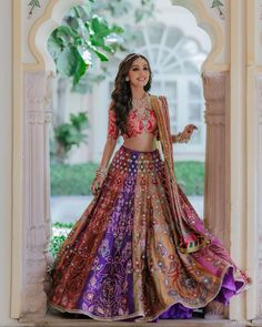 a woman in a purple and gold lehenga is posing for the camera with her hands on her hips