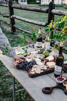 a man standing next to a wooden table filled with food and wine bottles on top of it