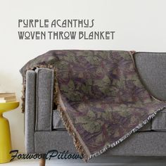 a couch with a blanket on top of it in front of a wall that says, purple acanthus woven throw blanket