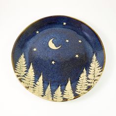 a blue plate with trees and the moon painted on it's side, against a white background