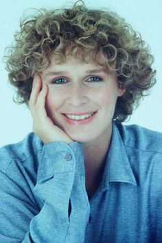 a woman with curly hair is smiling and posing for the camera while wearing a blue shirt