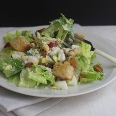 a white plate topped with lettuce salad and croutons next to a fork