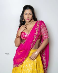 a woman in a yellow and pink lehenga posing for the camera with her hands on her hips