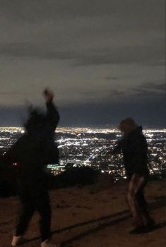 two people standing on top of a hill at night with the city lights in the background