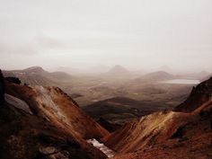 two people standing on top of a mountain looking out at the valley and mountains in the distance