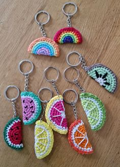 crocheted fruit keychains are arranged on a wooden surface, including one with a rainbow in the middle