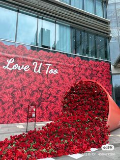 a giant red rose sculpture in front of a building with the words love u too written on it