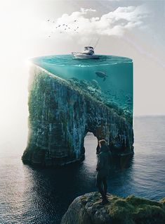 a man standing on top of a cliff in the ocean with a boat under water