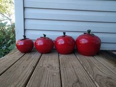 three red apples sitting on top of a wooden table next to each other in front of a house