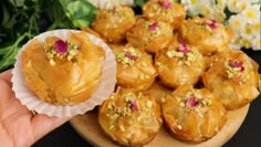 a hand holding a cupcake next to a plate of muffins with flowers in the background